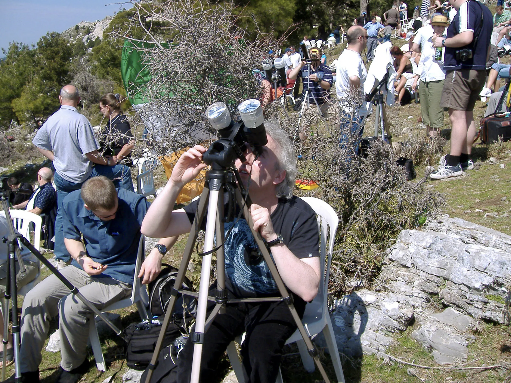 A woman looks at the Sun through binoculars that have been fitted with solar filters. Binoculars and telescopes can only be used to look at the Sun when used with solar filters specially designed for that purpose.