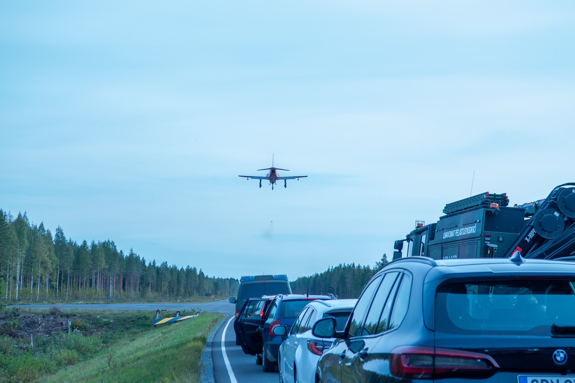 A photo of an airplane flying over a row of cars parked on a highway.