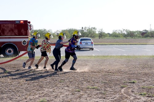 Four 17th Civil Engineer Squadron Airmen drag a firehose into position during the Fire Muster, a timed challenge for base personnel to complete a series of fire-related activities at Goodfellow Air Force Base, Texas, Oct. 13, 2023.