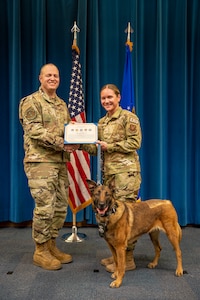 Man and woman pose with award next to dog.