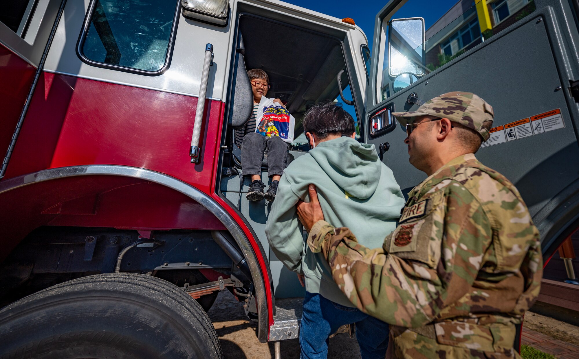 Senior Airman Michael Torres lifts students from Gunsan Jigok Elementary School onto a fire truck during a Fire Prevention Week educational event.