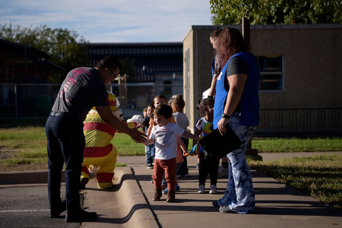 Youth from the Child Development Center at Goodfellow Air Force Base, Texas, high-five Sparky the Fire Dog and Daniel Chapa, Goodfellow Fire Department shift captain, Oct. 10, 2023.