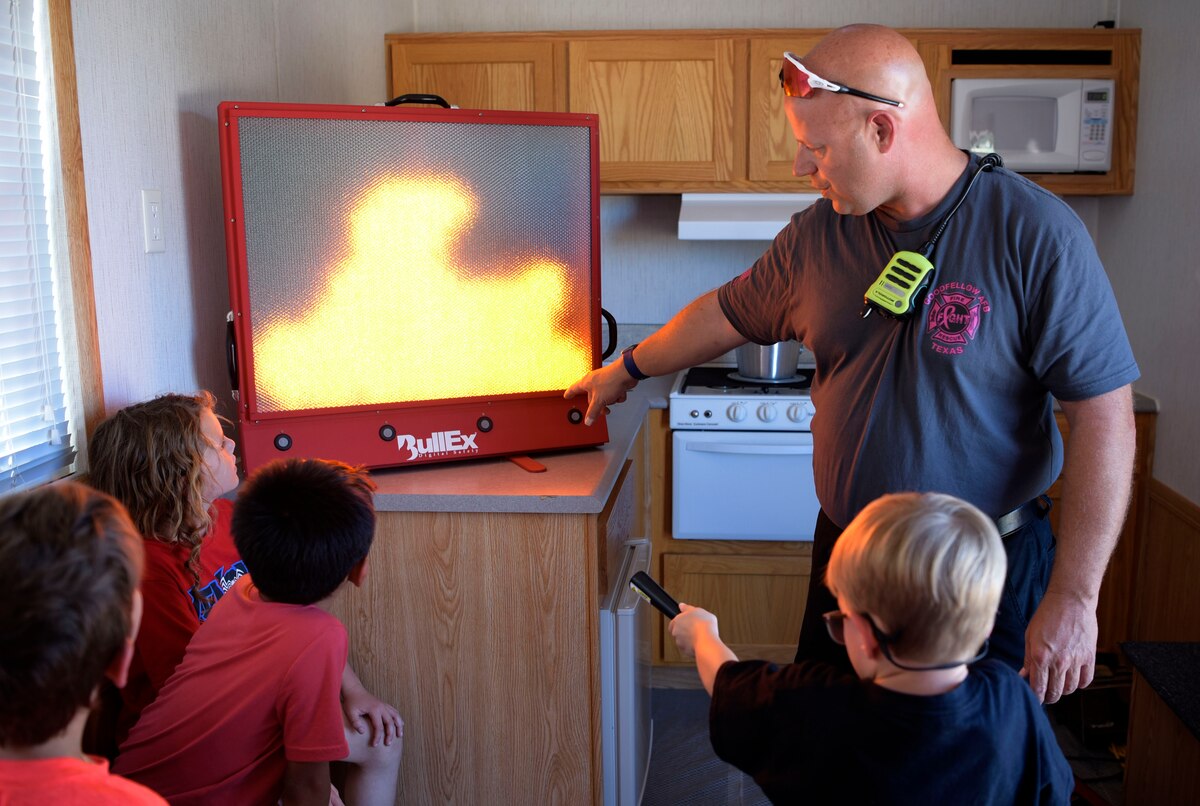 Brad Keibler, Goodfellow Fire Department fire inspector, shows a young boy where to point the fire extinguisher to put out the simulated fire on the screen during National Fire Week at Goodfellow Air Force Base, Texas, Oct. 11, 2023.