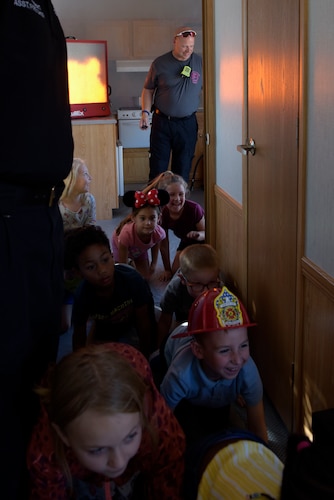 Youth from the school-age facility get low and crawl to safety as simulated smoke is seen on one side of the Fire Prevention Trailer during National Fire Week at Goodfellow Air Force Base, Texas, Oct. 11, 2023.
