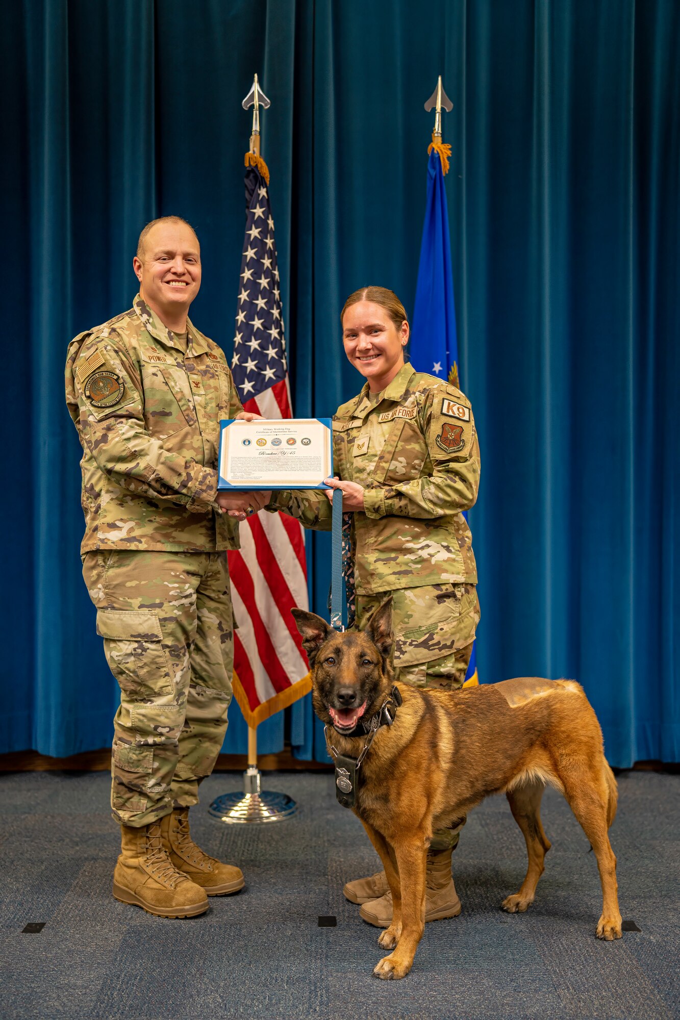 Man and woman pose with award next to dog.