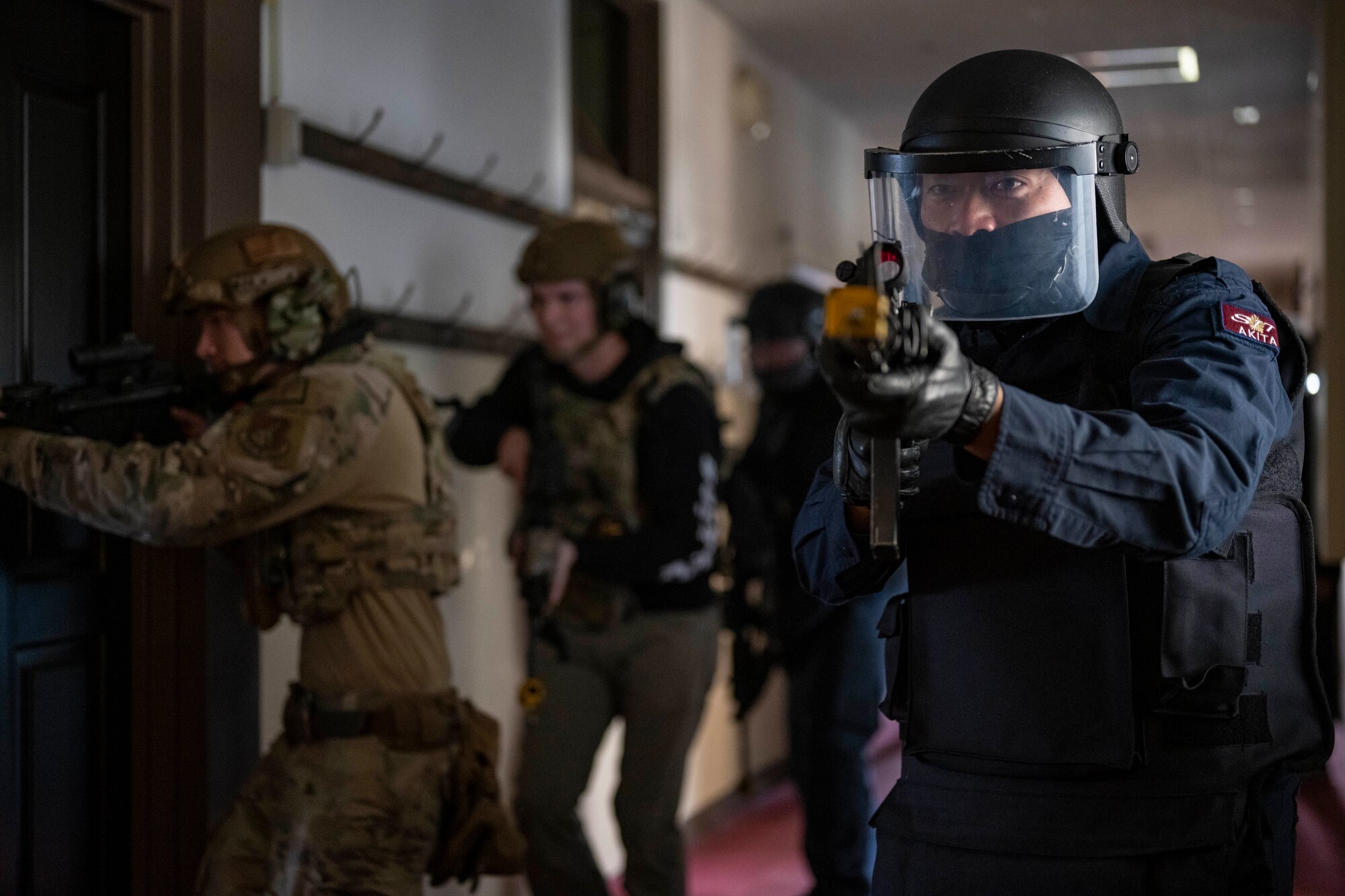 Police members conduct close-quarter combat training in a dark hallway.