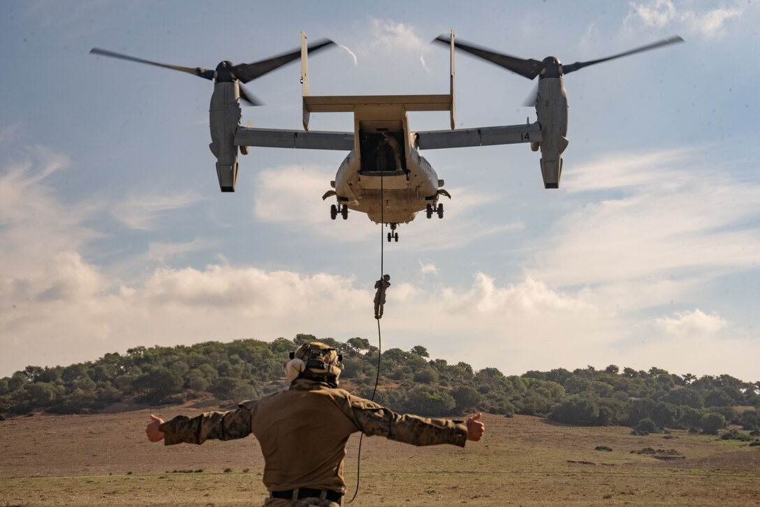 A U.S. Marine with Combined Anti-armor Team Red, Weapons Company, Battalion Landing Team 1/6, 26th Marine Expeditionary Unit (Special Operations Capable) (MEU(SOC)) gives the signal for the Marines to begin fast roping out of an MV-22 Osprey at Sierra del Retin Training Camp, Oct. 6, 2023. The San Antonio-class amphibious transport docking ship USS Mesa Verde, assigned to the Bataan Amphibious Ready Group and embarked 26th Marine Expeditionary Unit (Special Operations Capable) (MEU(SOC)), under the command and control of Task Force 61/2, is on a scheduled deployment in the U.S. Naval Forces Europe area of operations, employed by U.S. Sixth Fleet to defend U.S., Allied, and partner interests. (U.S. Marine Corps photo by Cpl. Michele Clarke)