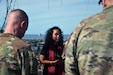 A woman speaks to two men wearing Army uniforms in an outdoor setting.