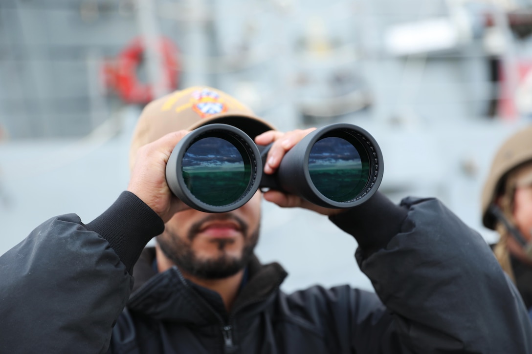 A sailor looks through a pair of binoculars.