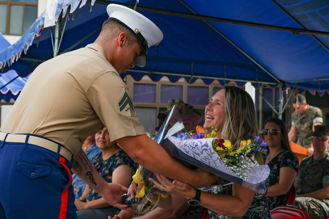 A Marine presents a bouquet of flowers to the wife of a sailor.