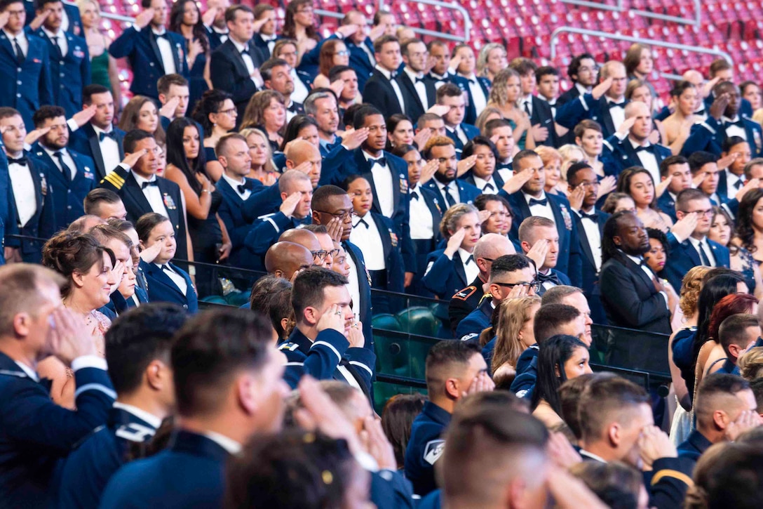 Airmen salute and civilians place their hands over their chest while standing in stands.