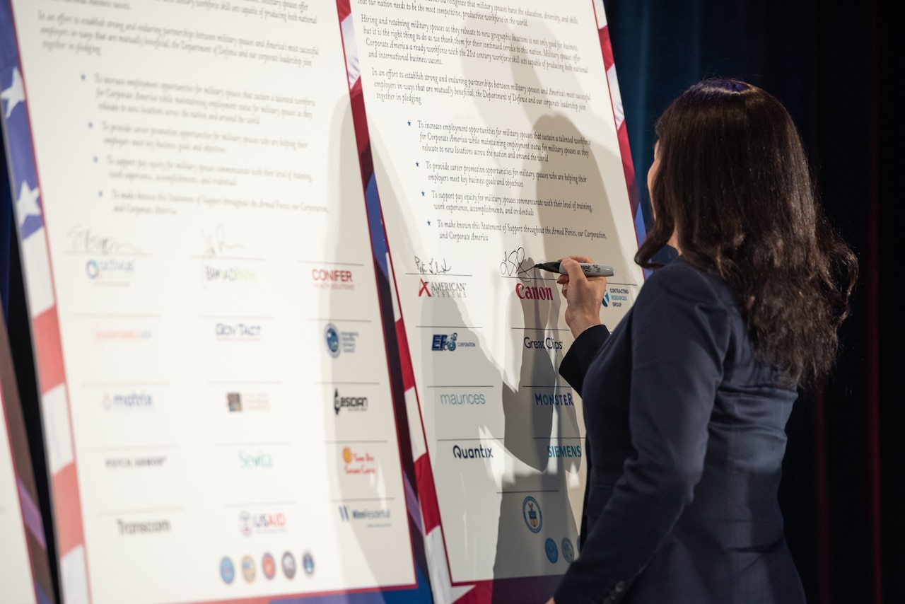 A person signs a poster-sized document on a easel.