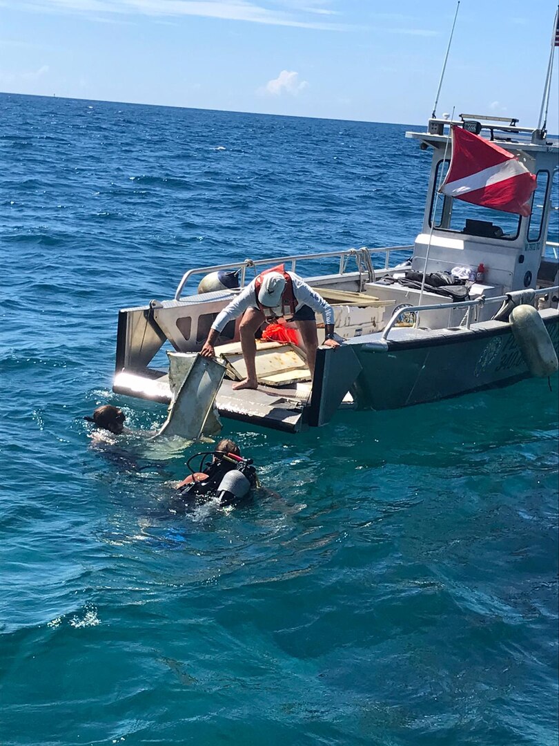 A dive tender takes collected debris from divers and bring it aboard the Bonnie G for disposal off Cyril E. King Airport, St. Thomas, Oct. 15, 2023. Divers removed approximately 2,500 lbs of debris from the ocean floor. (U.S. Coast Guard photo)