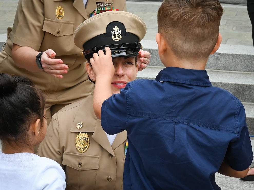 230929-N-VP266-0269 WASHINGTON (Sep. 29, 2023) Chief Master at Arms Larissa Carman, assigned to Naval District Washington (NDW), receives her chief anchors and new cover from her children during the NDW chief pinning ceremony at the U.S. Navy Memorial, September 29, 2023. The rank of chief petty officer was officially established April 1, 1893, and holding the title "Chief" means a Sailor has achieved senior non-commissioned officer status. (U.S. Navy photo by Mass Communication Specialist 2nd Class Griffin Kersting)