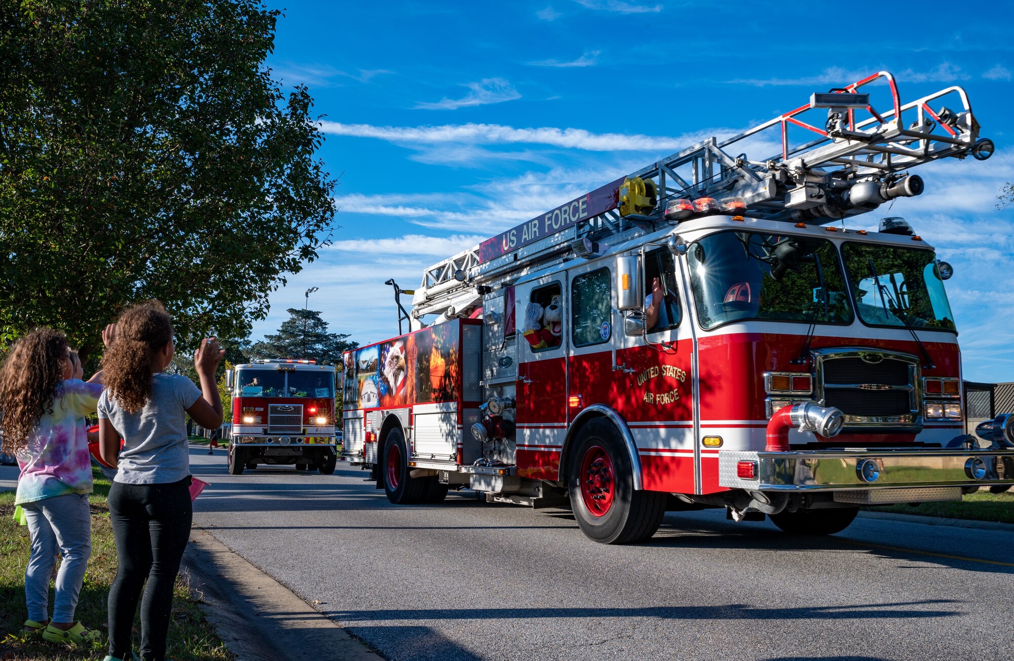 Young children wave at 436th Civil Engineer Squadron Airmen driving by in an emergency service vehicle during the 2023 Fire Prevention Week Parade at Dover Air Force Base, Delaware, Oct. 13, 2023. Fire Prevention Week is a nation-wide observation that teaches people how to stay safe in case of a fire. (U.S. Air Force photo by Airman 1st Class Amanda Jett)