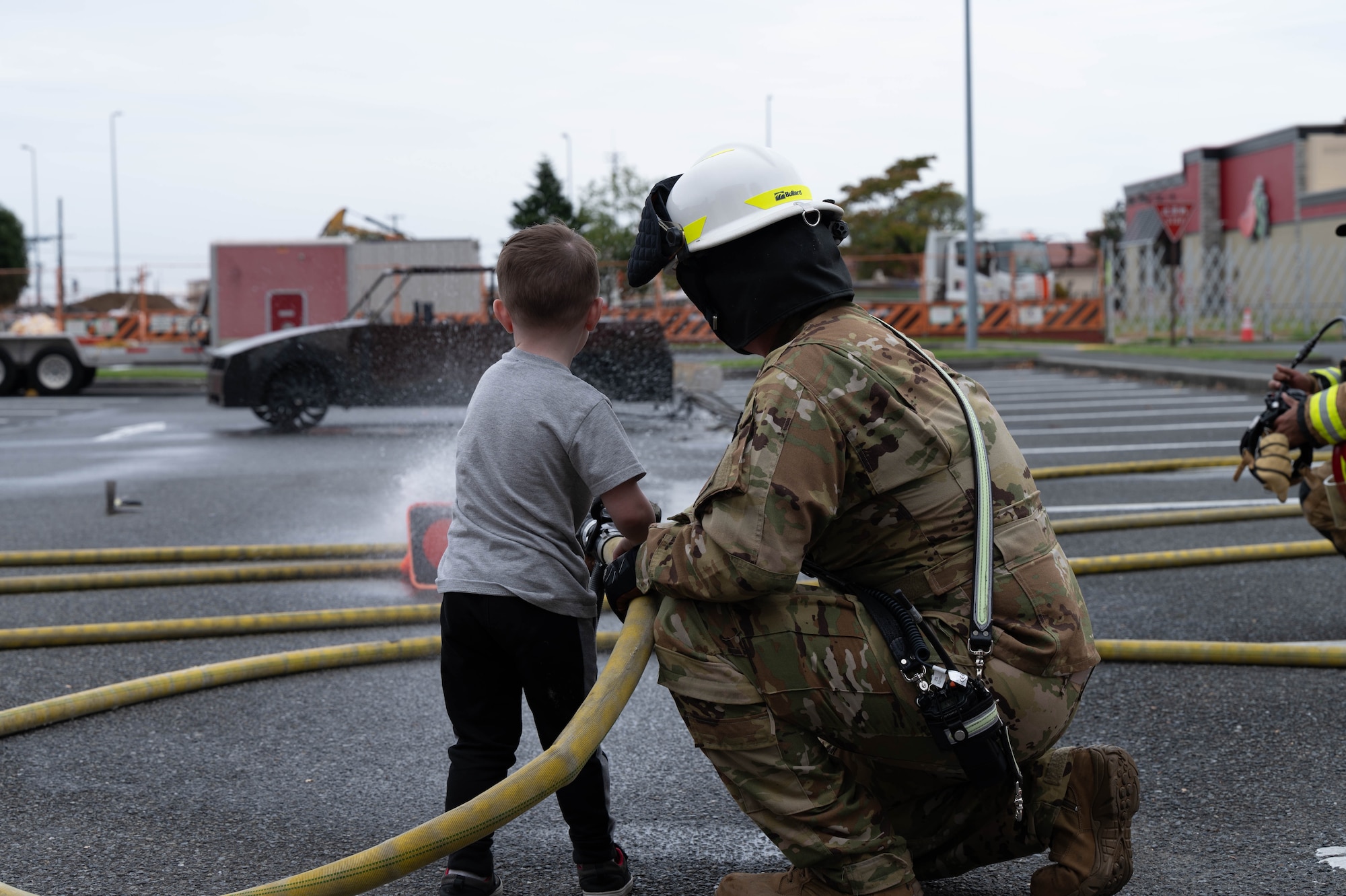 A firefighter sprays a firehose with a child.