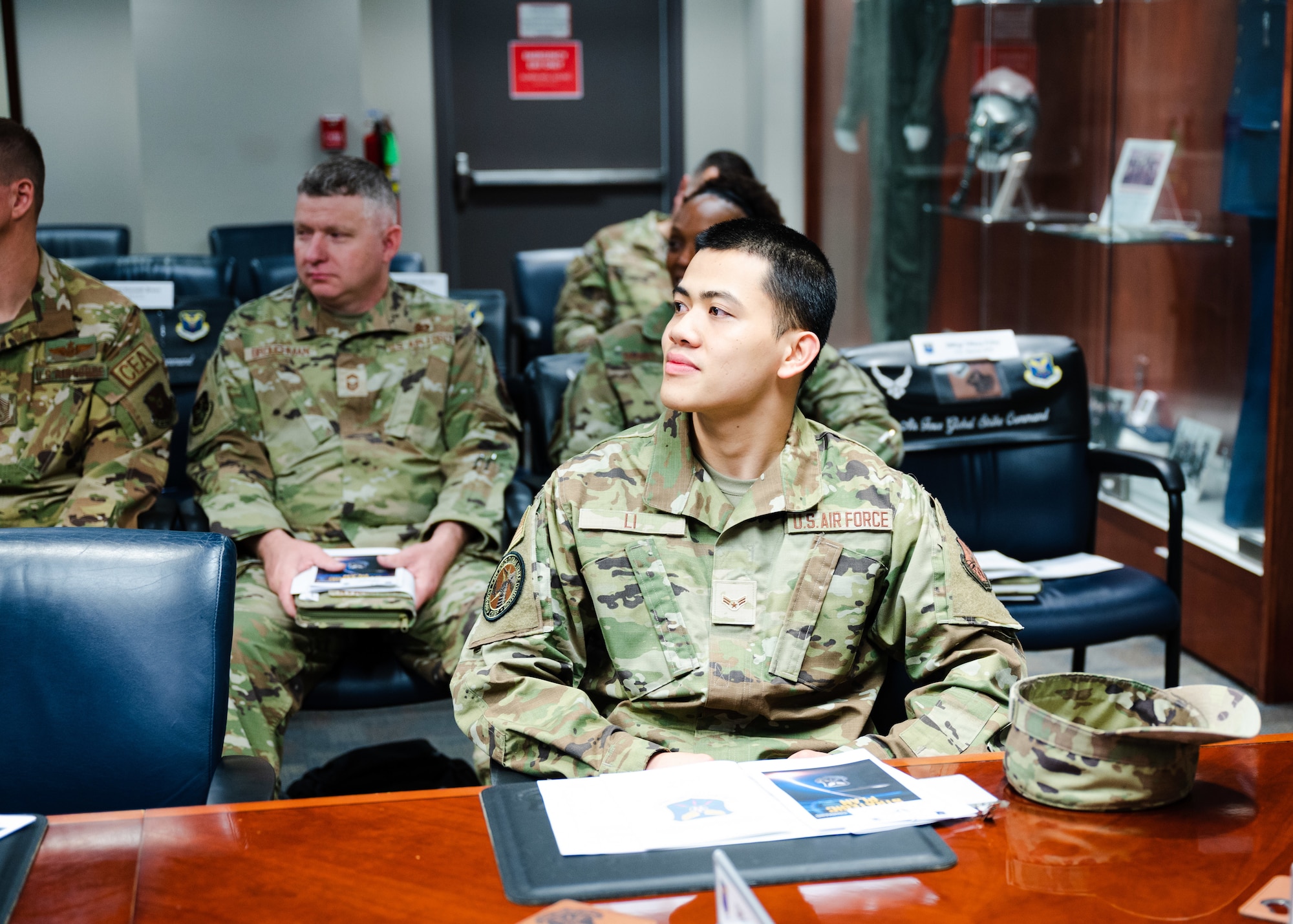 someone sits at a desk for a meeting with other people sitting behind them also in the meeting