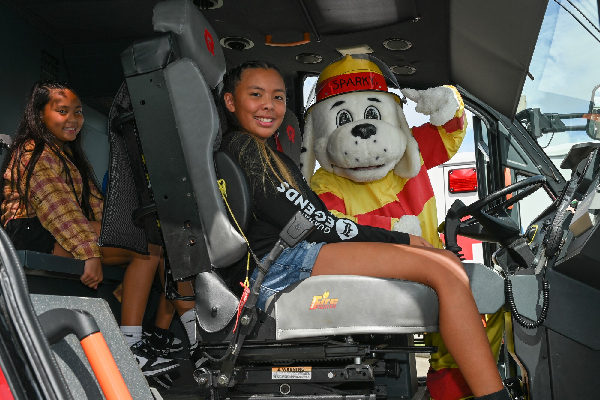 Sparky the Fire Dog poses for a photo with children of a military family inside of an airport rescue firefighting truck