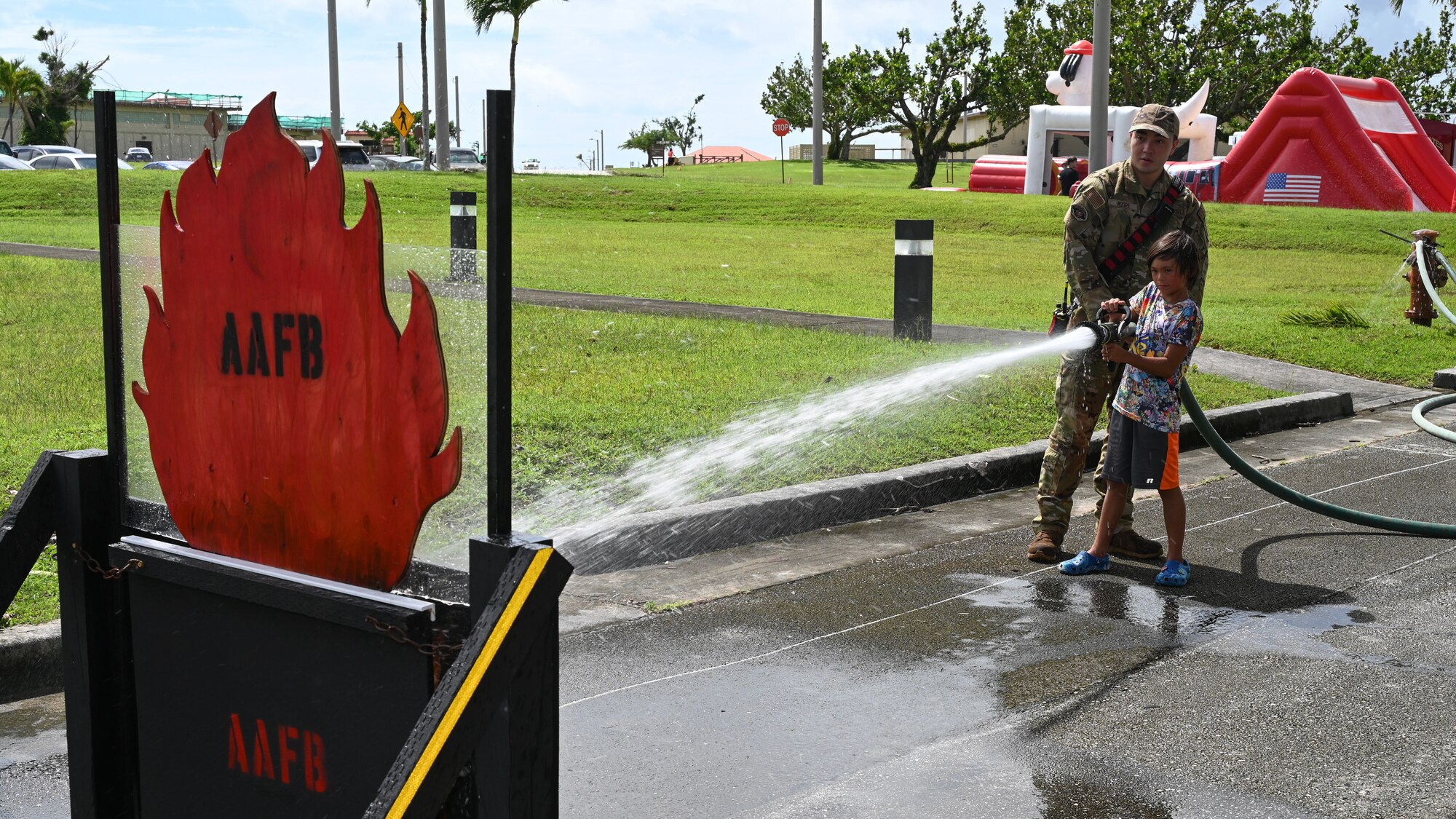 An Airman assists a child with spraying water from a water hose to a simulated fire.