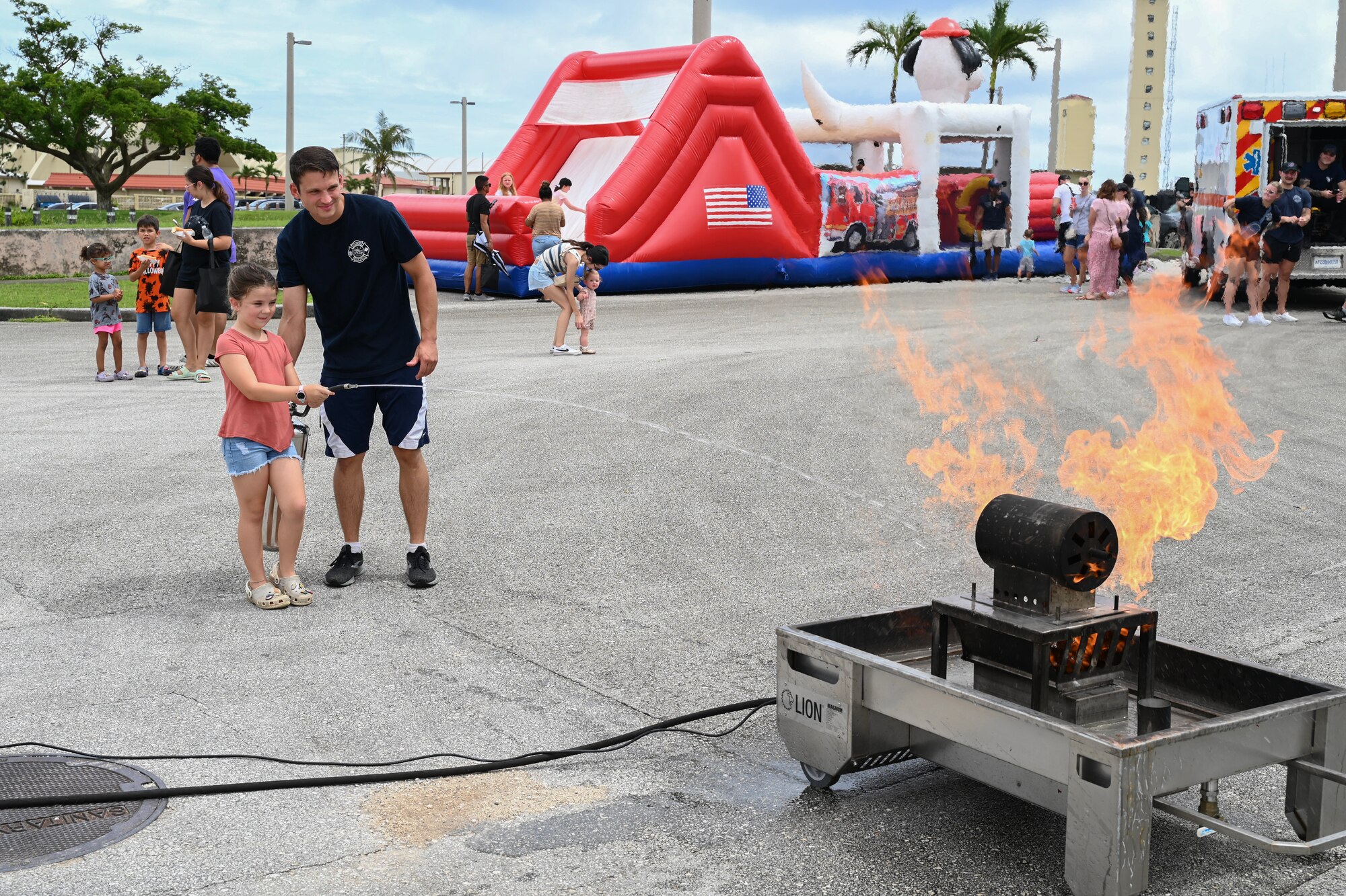A fire inspector assists a child with taking out a simulated fire with fire extinguisher.