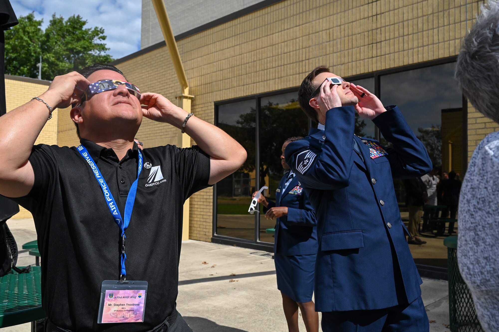 Stephen Ynostrosa, Randolph Brooks Federal Credit Union vice president of business development, and Master Sgt. Michael Lahrman, 433rd Airlift Wing Public Affairs non-commissioned officer in charge of media operations, view the solar eclipse event after the Honorary Commanders’ Induction Ceremony on Joint Base San Antonio-Lackland Texas, Oct. 15, 2023. Special solar eclipse glasses were provided to attendees in order to partake in the solar eclipse event after the induction ceremony. (U.S. Air Force photo by Staff Sgt. Adriana Barrientos)