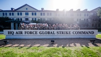 A group of people stand in front of a building's sign that says "HQ Air Force Global Strike Command"