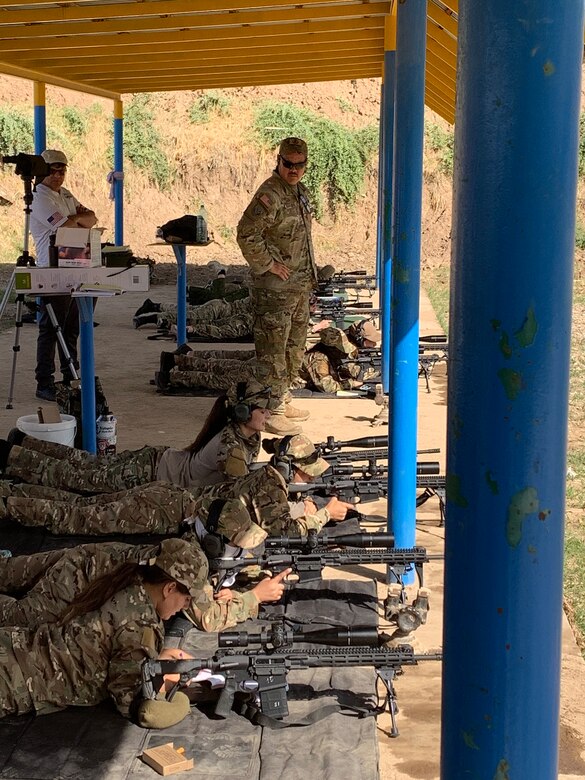 Service members lie on the ground firing weapons at a target.