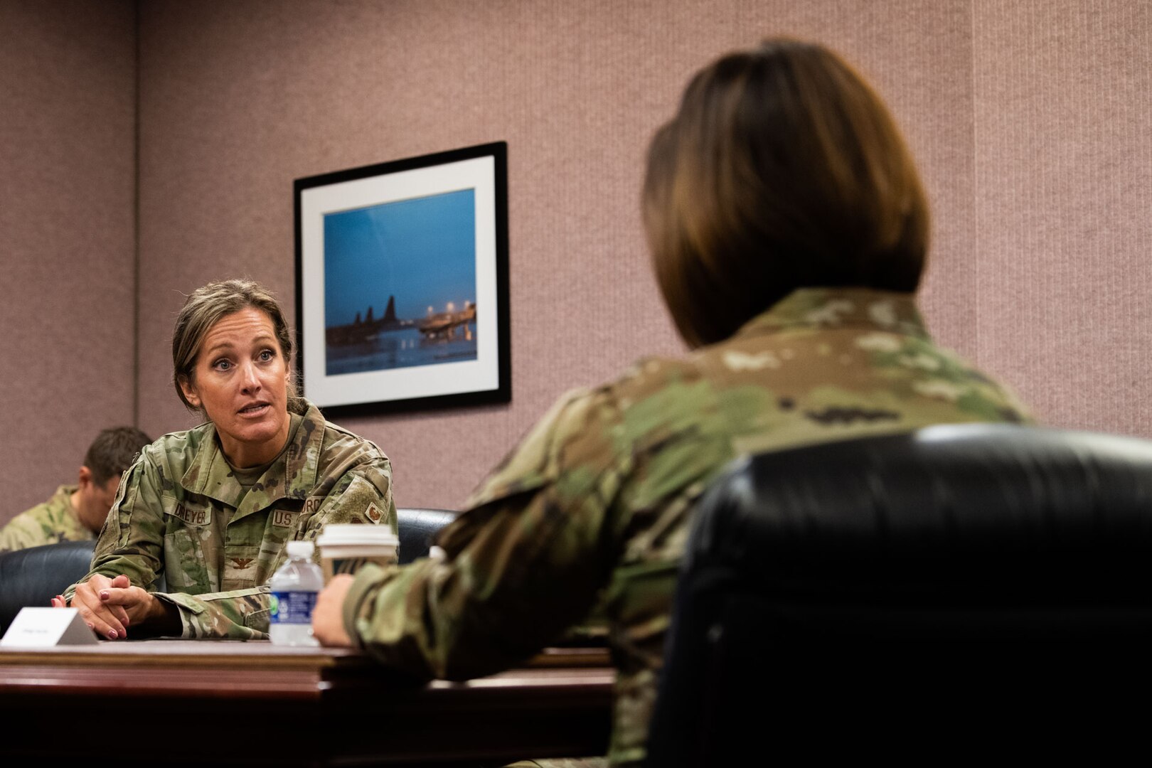 two women Airmen speak in a meeting room