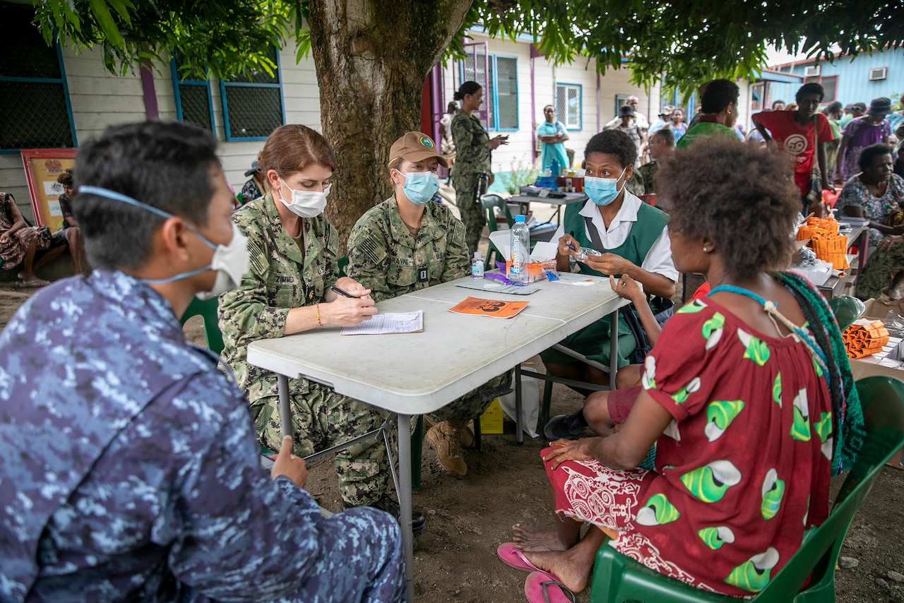 Sailors sit around a table and take notes while talking with civilians.