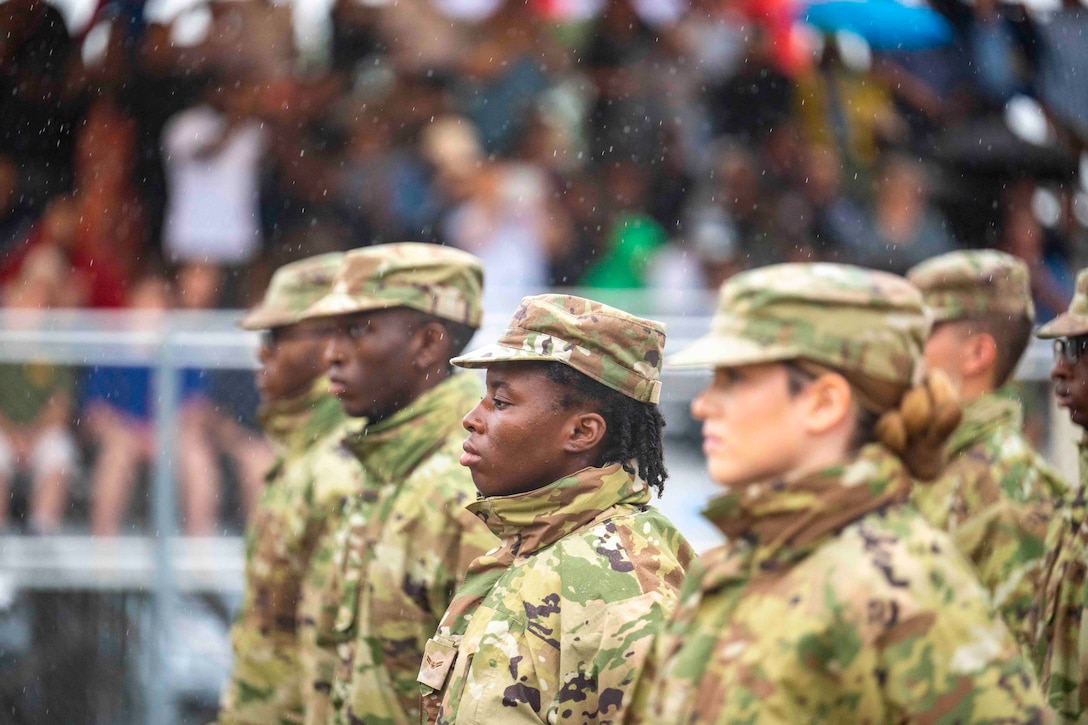 Airmen stand in formation in front of a crowd as rain falls.