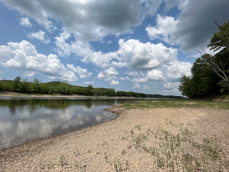 The Osage River can be seen with rocks in the foreground and trees and a blue sky in the background.