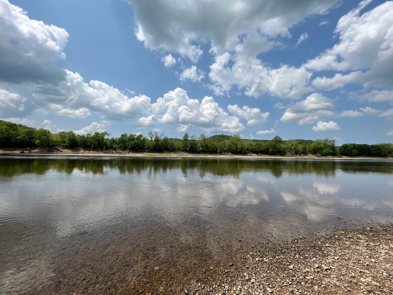 The Osage River can be seen with rocks in the foreground and trees and a blue sky in the background.