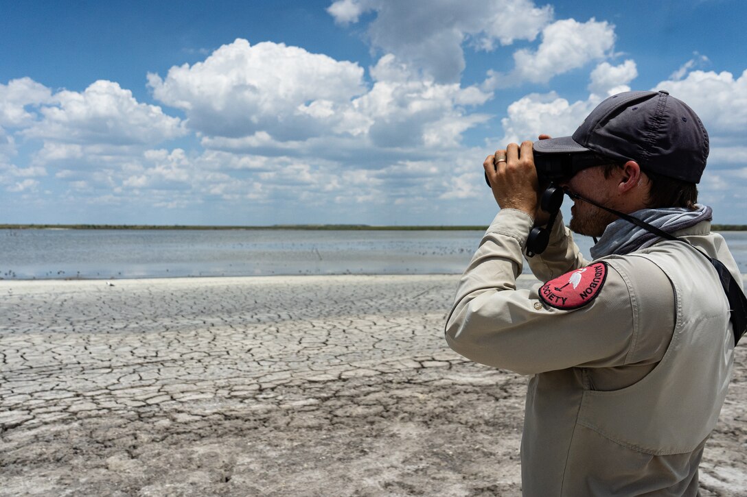 A representative from the National Audubon Society, looks out through binoculars at wading birds.