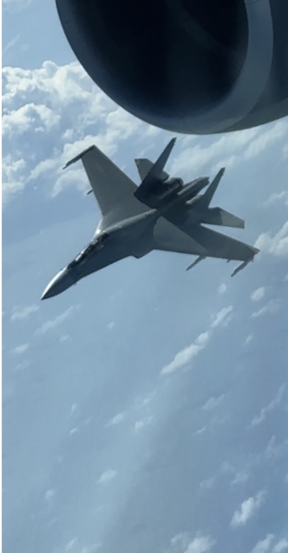 An aircraft flies against a blue sky with clouds.