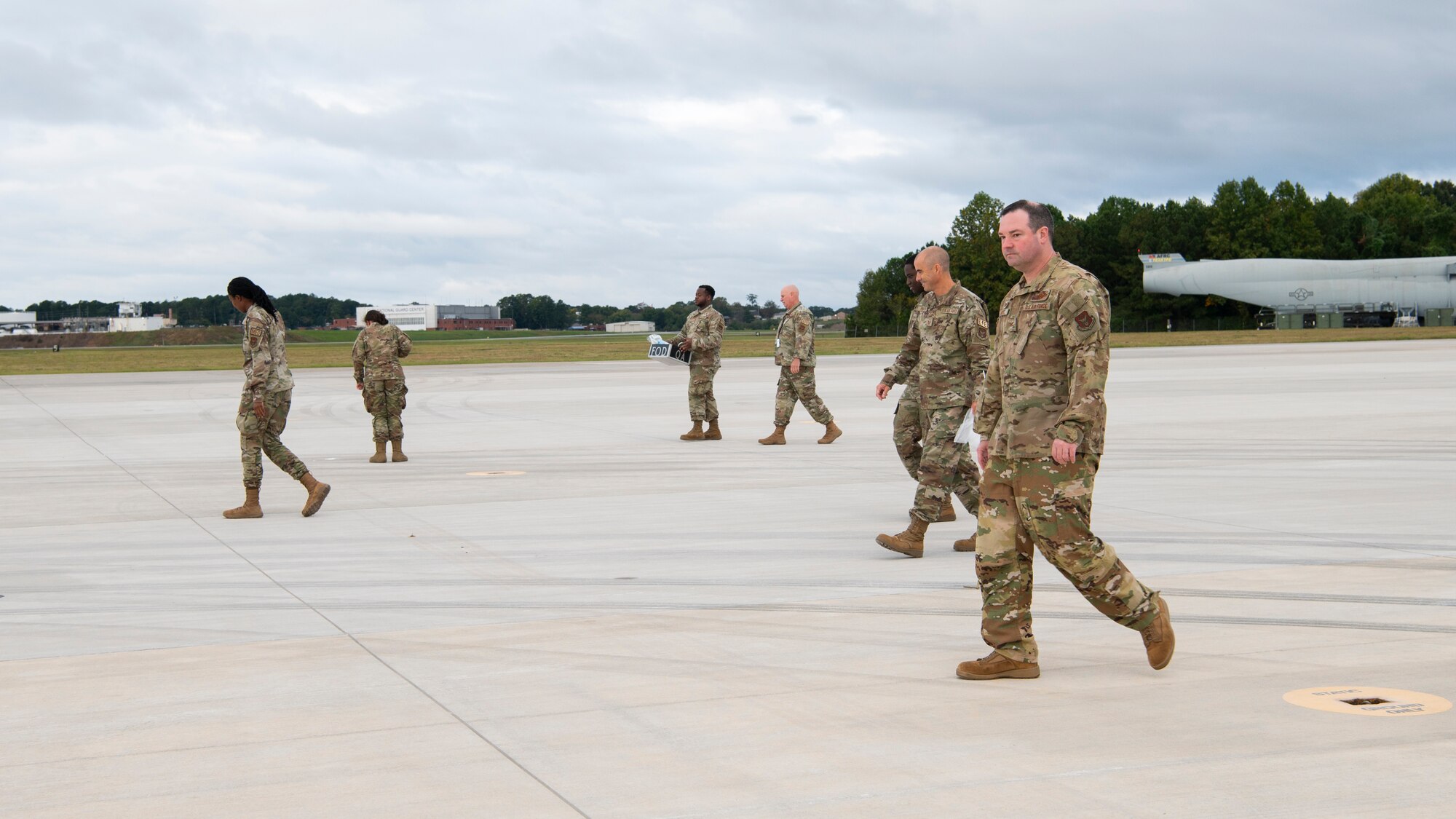 people in military uniforms gather debris from a flightline and dispose of it into a garbage bag