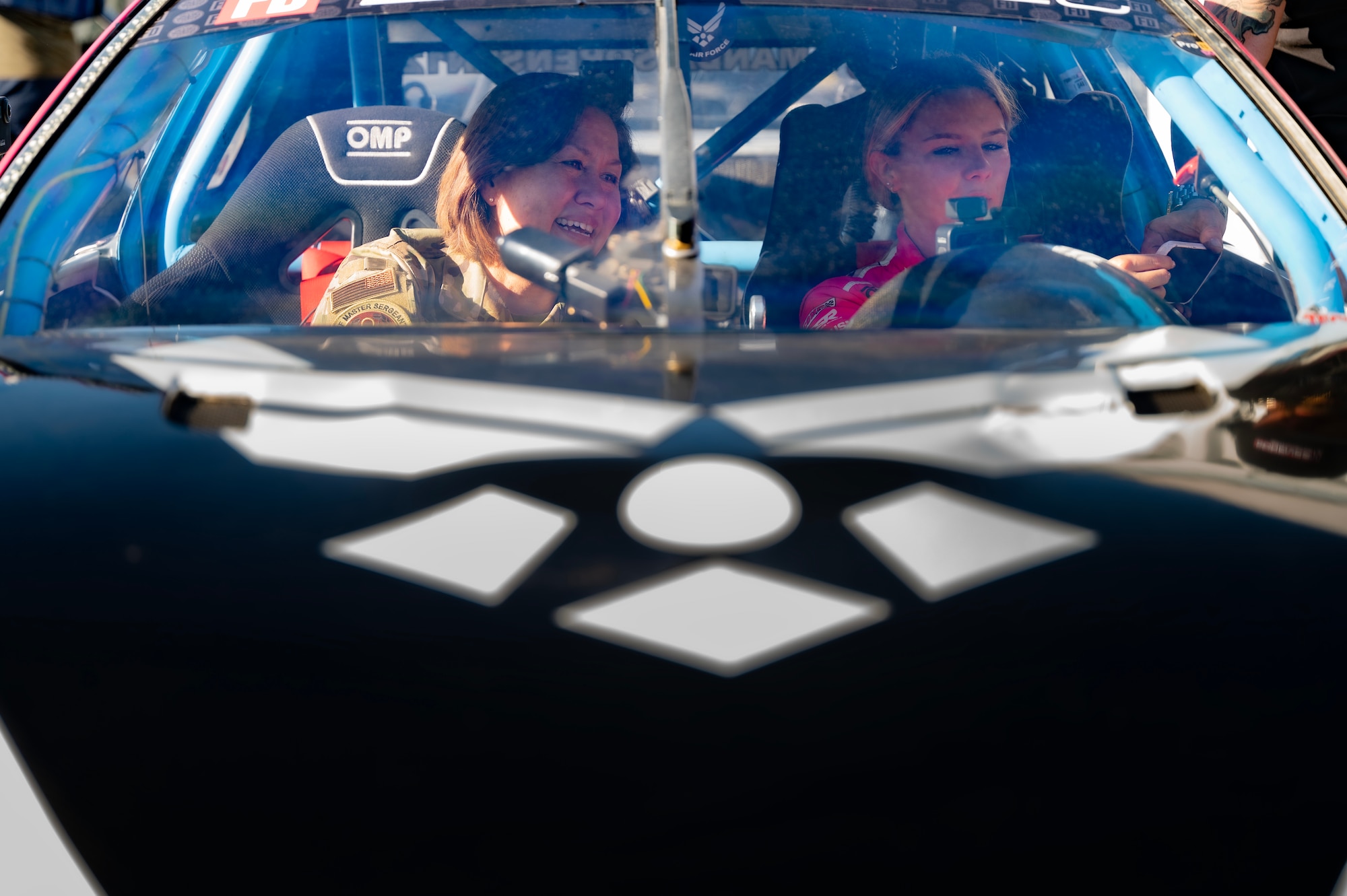 woman in uniform sits in racecar next to driver