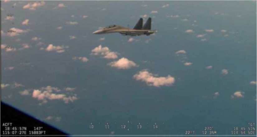 A jet flies near another aircraft, partly visible in the foreground.