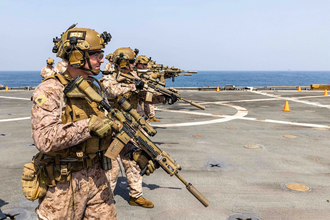 Service members wearing battle gear handle rifles aboard a Navy ship.