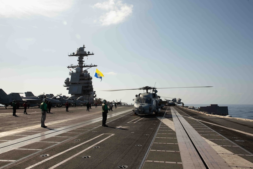 Sailors wearing flight deck gear stand on the flight deck of a Navy aircraft carrier.