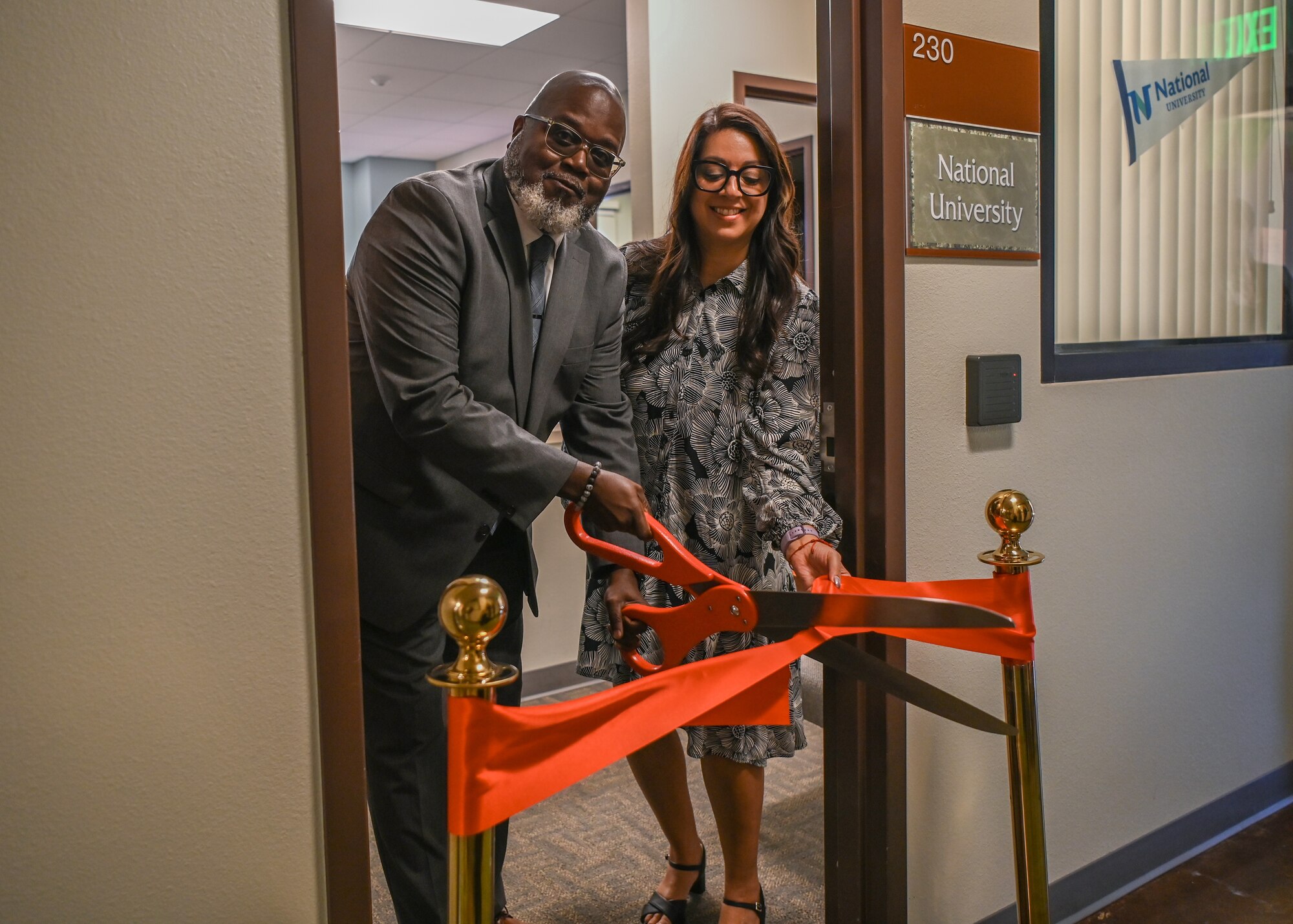 A college associate vice president and senior director pose for a photo and cuts their school's ribbon during an education center open house.
