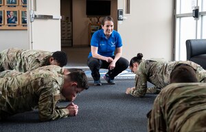 U.S. Air Force Lt. Col. Ember Ryals, operational support team flight commander, times Airmen holding a plank position at Joint Base Lewis-McChord, Wash., June 8, 2023. An operational support team is embedded with the 627th Communications Squadron; an OST is a small, multidisciplinary health and human performance outreach team composed of musculoskeletal and mental health clinicians. (U.S. Air Force photo by Staff Sgt. Rachel Williams)