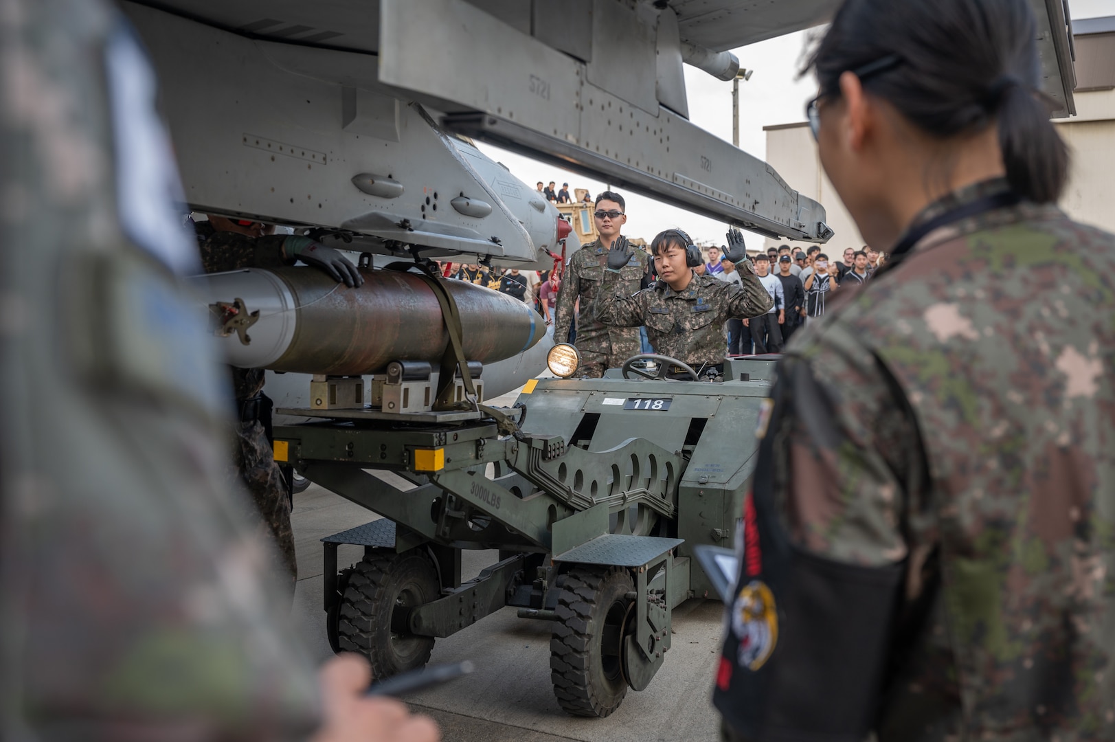 A load crew member, ensures the munition loading vehicle remains steady as his teammates coordinate the position of a munition during Pen Fest, the annual bilateral munitions load crew competition at Kunsan Air Base