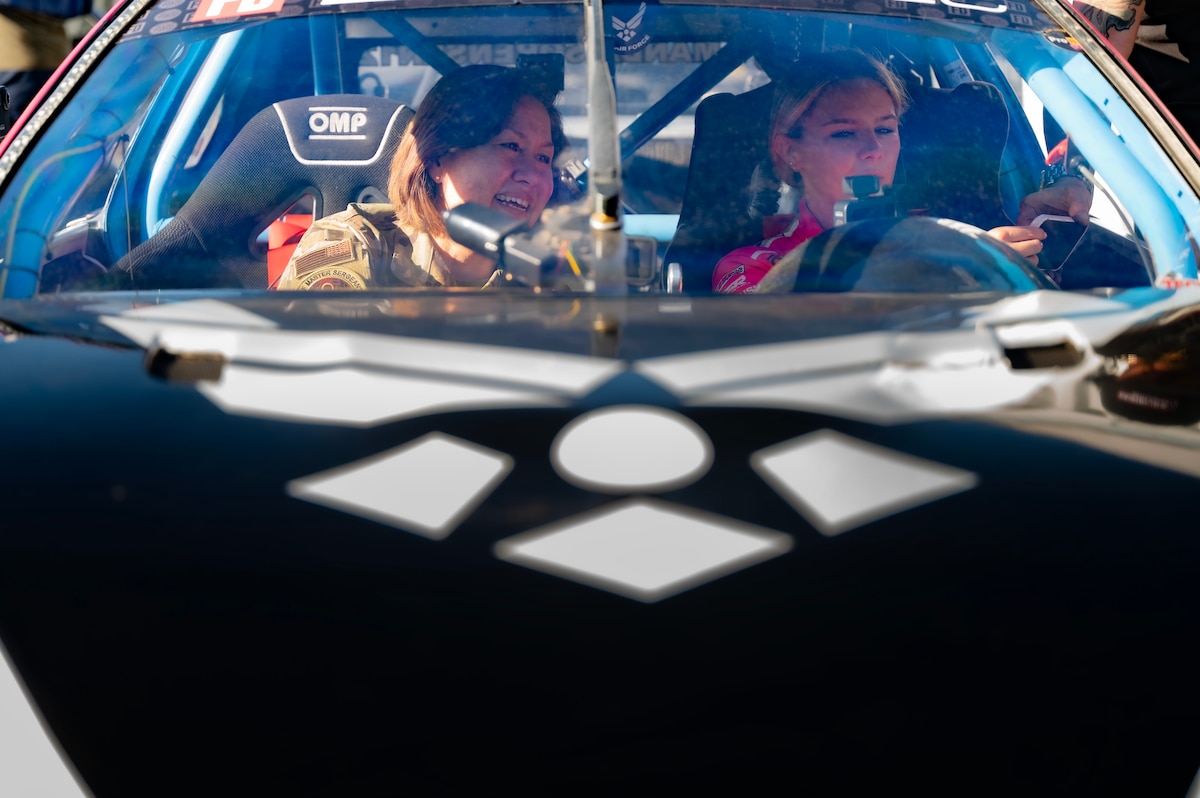 woman in uniform sits in racecar next to driver