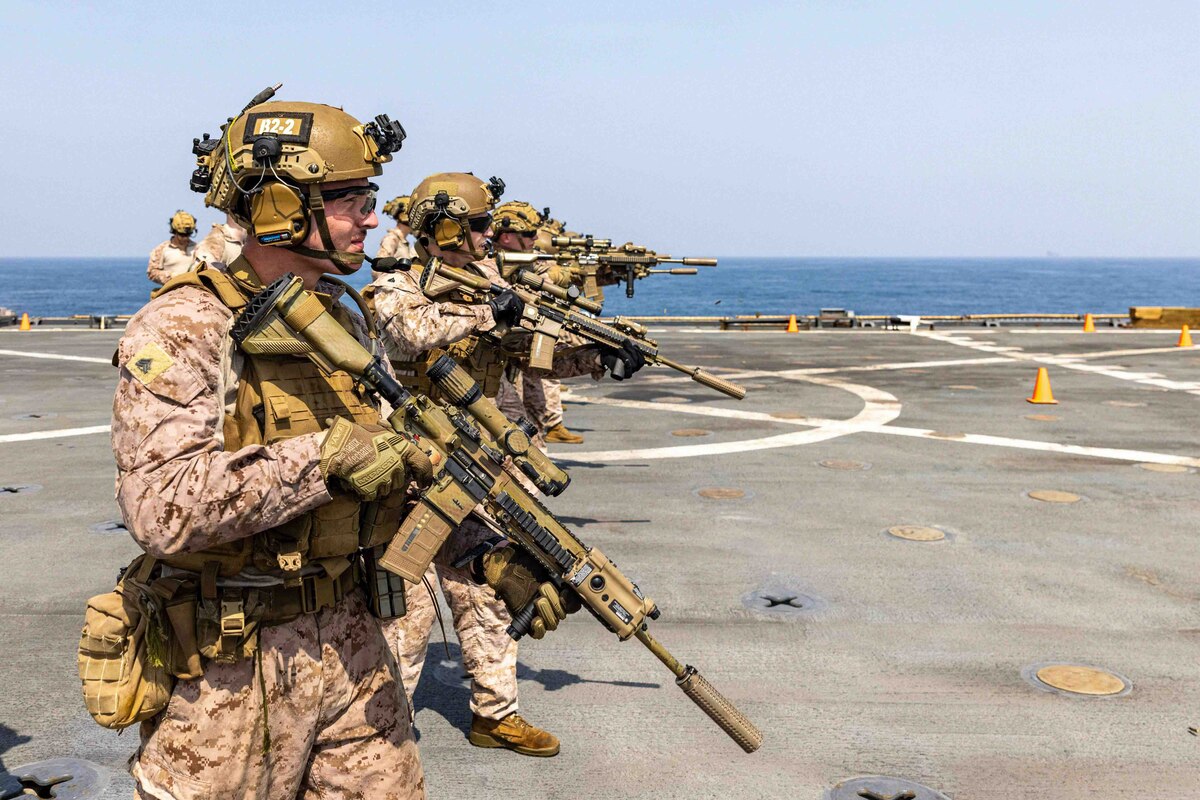 Service members wearing battle gear handle rifles aboard a Navy ship.