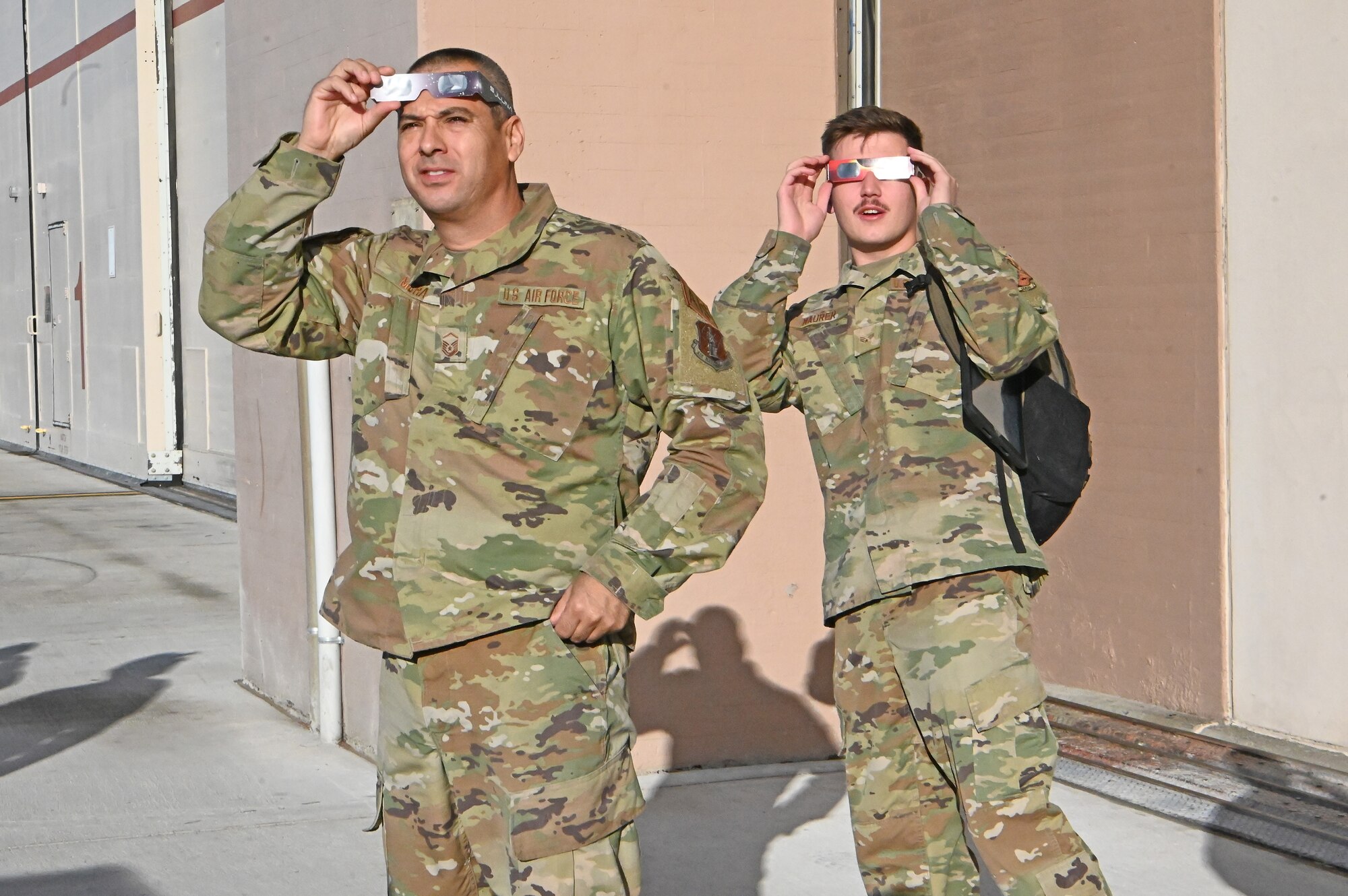 U.S. Air Force Master Sgt. Rudy Mora and Senior Airman Peyton Maurer, 173rd Maintenance Group, peer toward the solar eclipse.