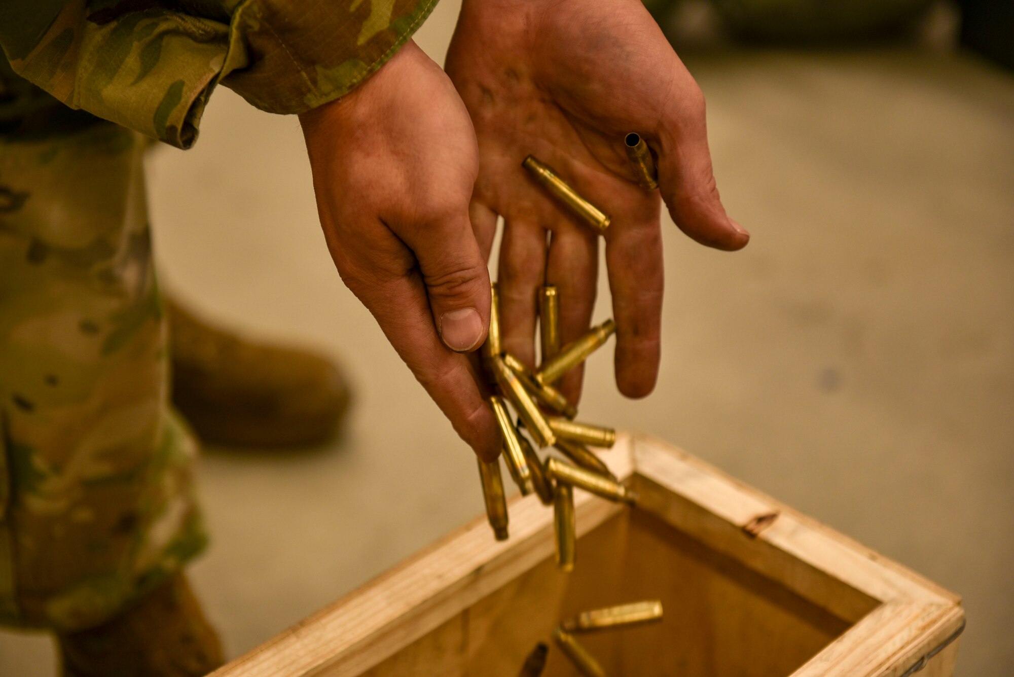 An Airman puts rifle bullet casings into a wooden box.