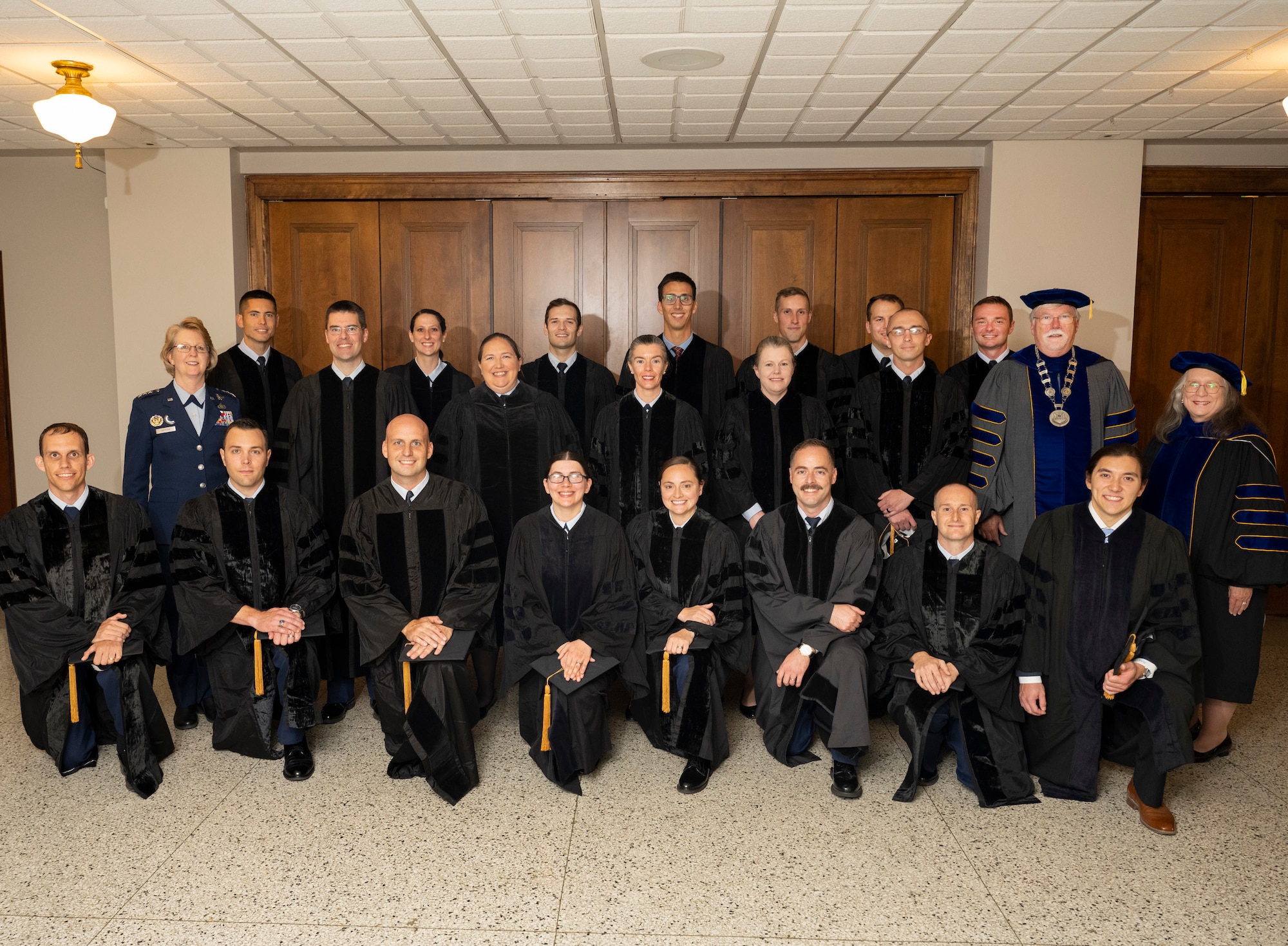 A group of 22 people in academic garb and one woman in Air Force uniform pose in a group photo.