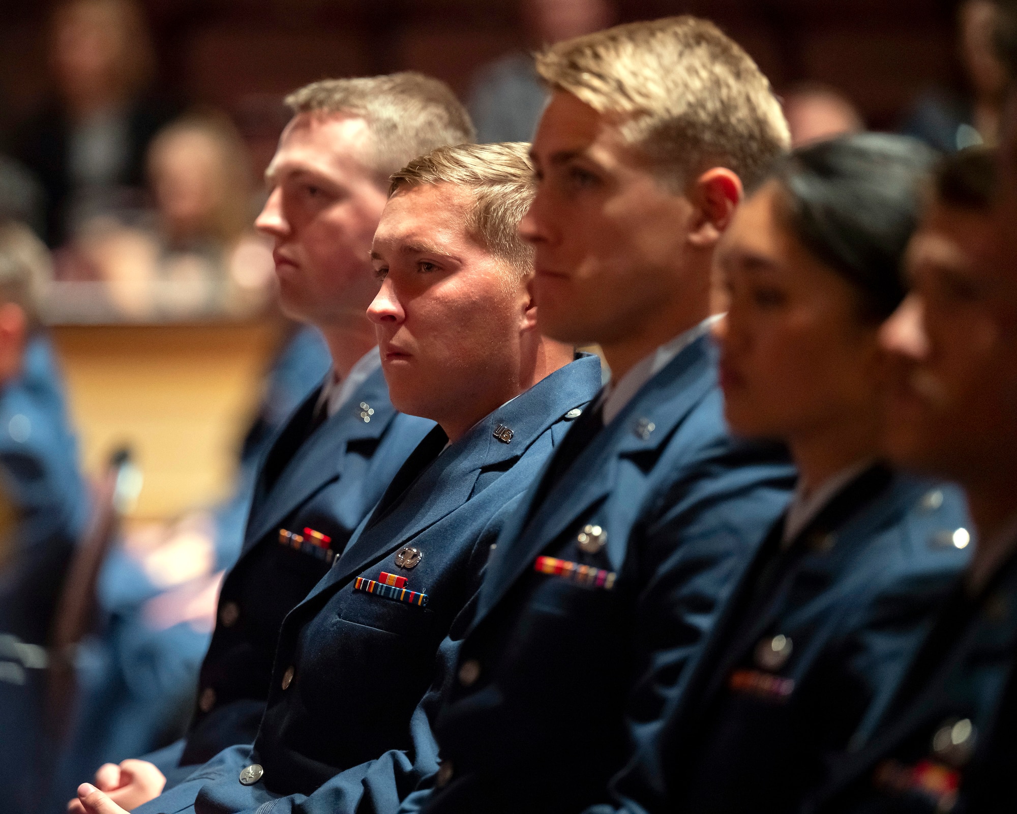 A row of people in Air Force dress uniform sit facing to the left.