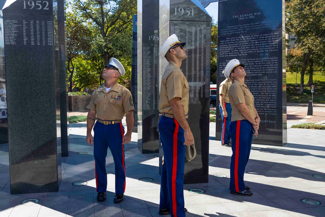 Marines walk through a monument that showcases writing on different pillars.