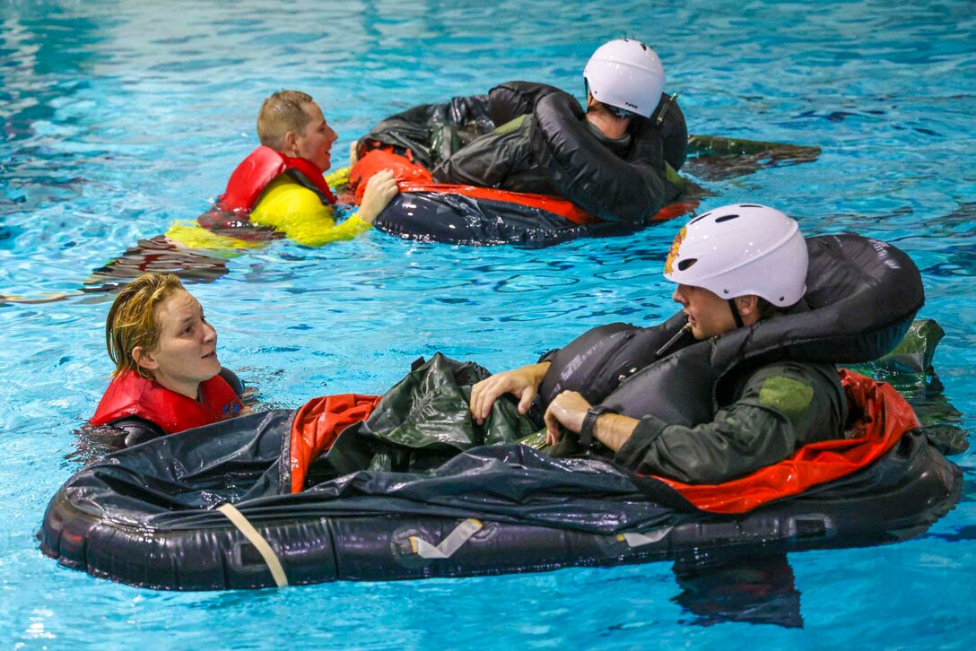 Two airmen in a pool help two others in small inflatable rafts.